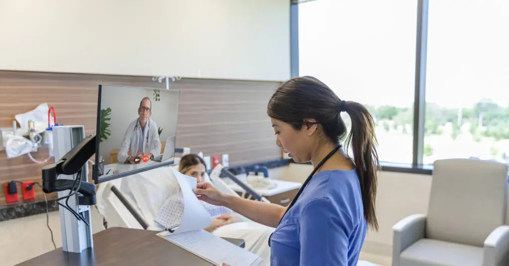 Nurse utilizing hybrid health capabilities discussing patient notes with a doctor via computer