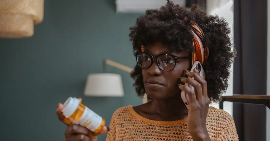 Woman speaking on a smartphone about her post-discharge prescription instructions while holding a medicine bottle