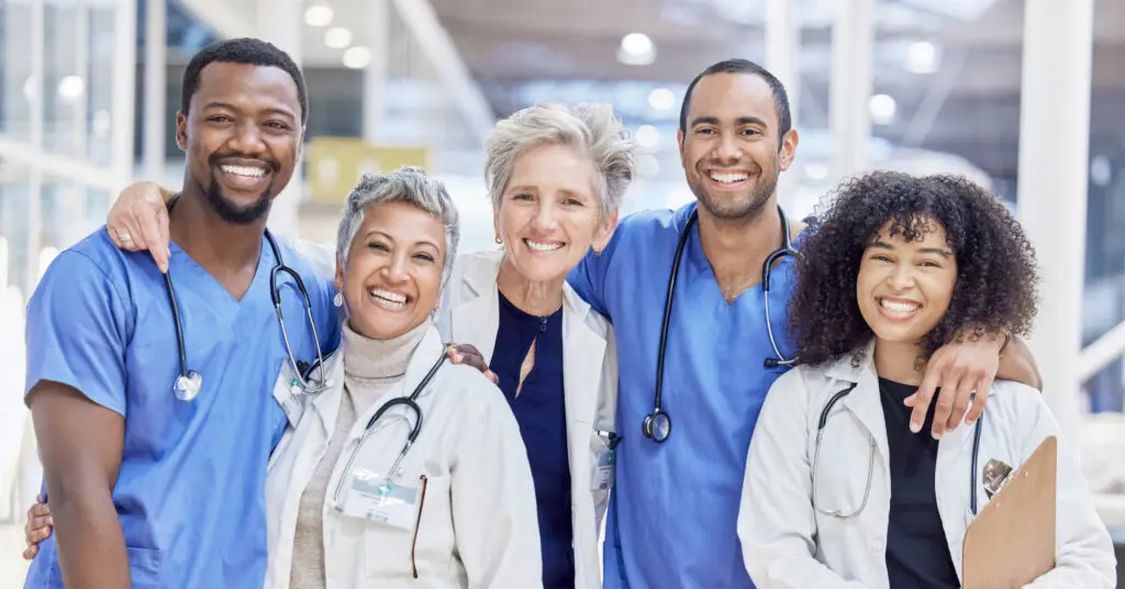 Several physicians in scrubs and lab coats laughing and smiling